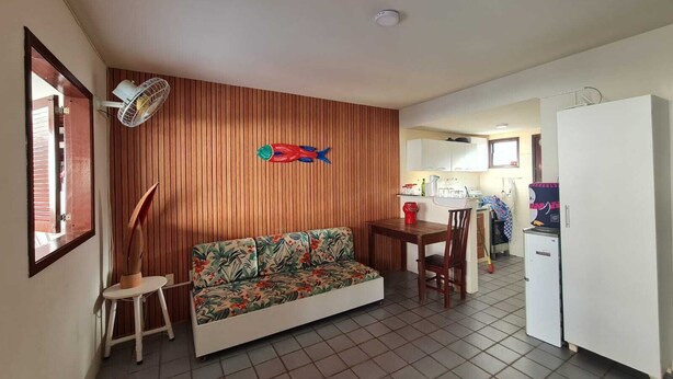 A compact living space with a wooden wall, a sofa, a dining table, and a kitchenette. - Retreat in Maragogi: 4 Bedrooms | Space & Leisure (Barra Grande)