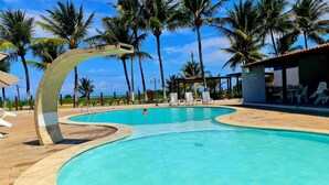A swimming pool with a curved edge, surrounded by palm trees and lounge chairs. - Retreat in Maragogi: 4 Bedrooms | Space & Leisure (Barra Grande)