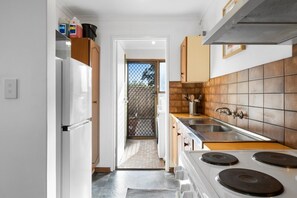 A kitchen with a stove, sink, cabinets, and a door leading to a balcony.