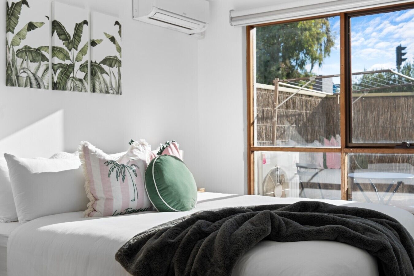 Een slaapkamer met een bed, kussens, een deken, een groot raam en een airconditioning.