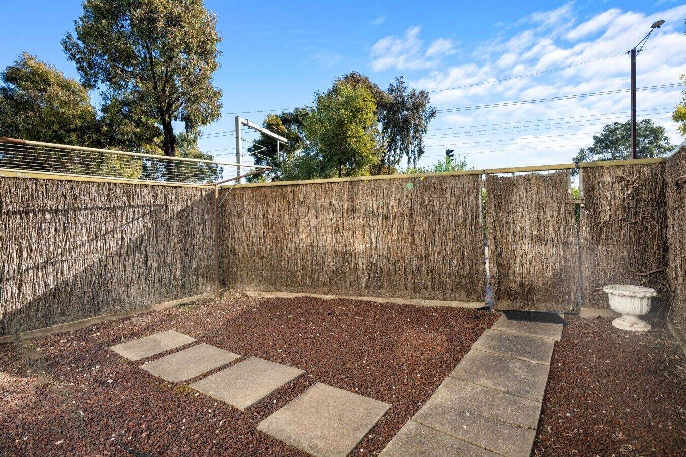 A fenced outdoor area with a gravel path and a stone bench.