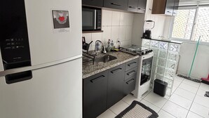 A modern kitchen with a refrigerator, microwave, sink, and a window with a view. - Ocean leisure (São Vicente)