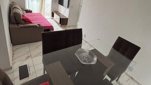 A modern living room with a glass dining table, a sofa, a TV, and a window with curtains. - Ocean leisure (São Vicente)