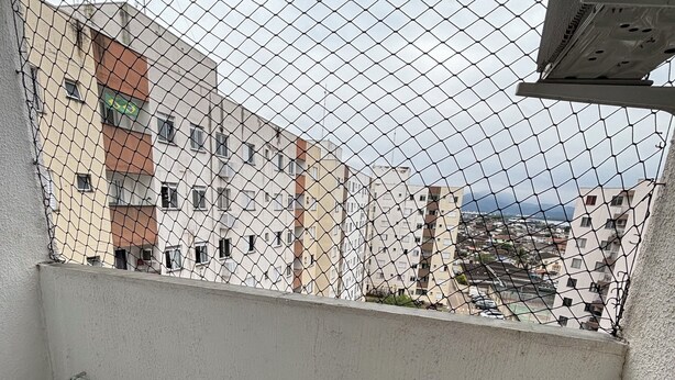 A balcony with a metal drying rack, a tiled floor, and a view of buildings through a chain-link fence. - Ocean leisure (São Vicente)
