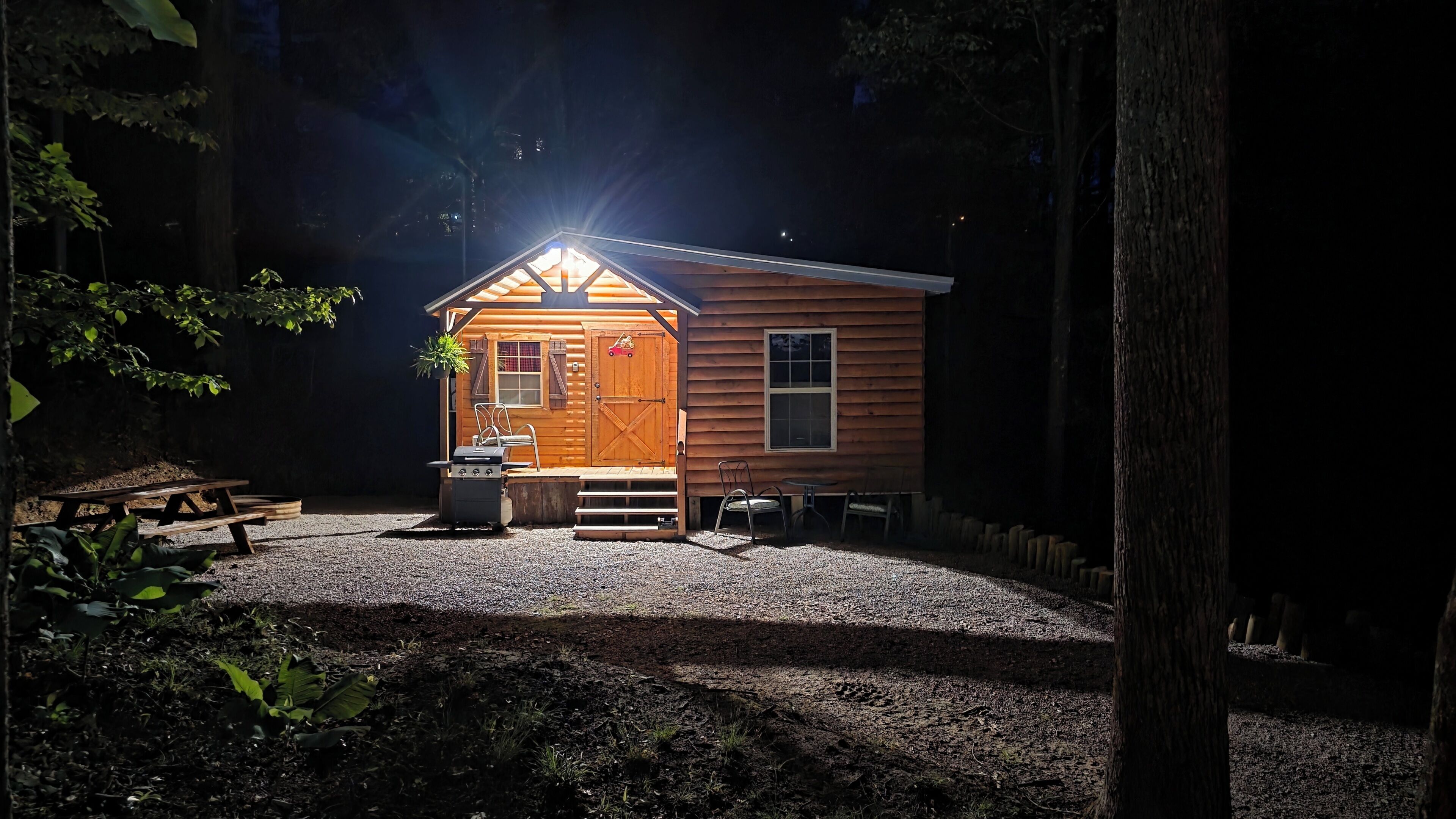 A small wooden cabin with a porch, a grill, and a picnic table.
