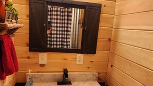 Un baño de cabaña de madera con un espejo grande, un lavamanos y tres luces fijadas a la pared.