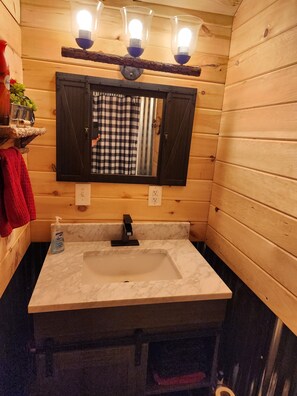 A wooden cabin bathroom with a large mirror, a sink, and three wall-mounted lights. - Tranquil 1-bedroom cabin with AC in charming Zoe (Zoe)