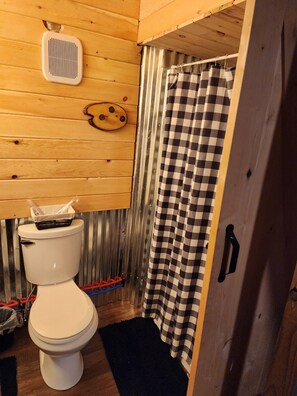 A wooden-paneled bathroom with a toilet, a shower curtain, and a vent on the ceiling. - Tranquil 1-bedroom cabin with AC in charming Zoe (Zoe)