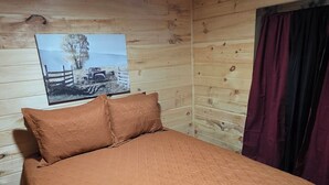 Una habitación de cabaña de madera con una cama, un cartel en la pared y una ventana con cortinas.