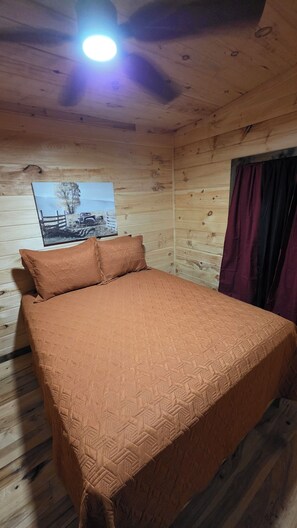 A wooden cabin room with a bed, a poster on the wall, and a window with curtains. - Tranquil 1-bedroom cabin with AC in charming Zoe (Zoe)