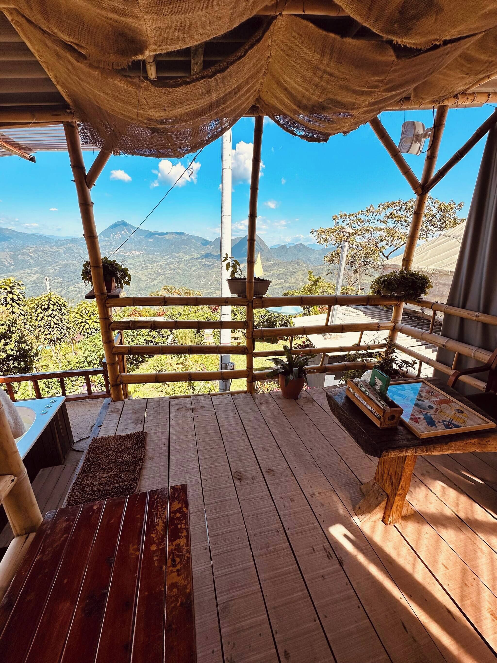 Terraza de madera con vista a montañas, baranda de bambú y plantas en macetas.