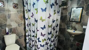 A bathroom with a stone wall, a white toilet, a sink, and a shower curtain with butterfly patterns.