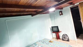 A bedroom with a bed, a television on a stand, a fan, and a wooden ceiling.