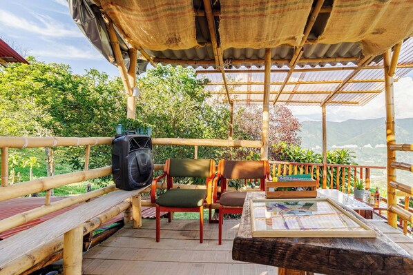 A covered outdoor seating area with chairs and a table, overlooking a lush landscape.