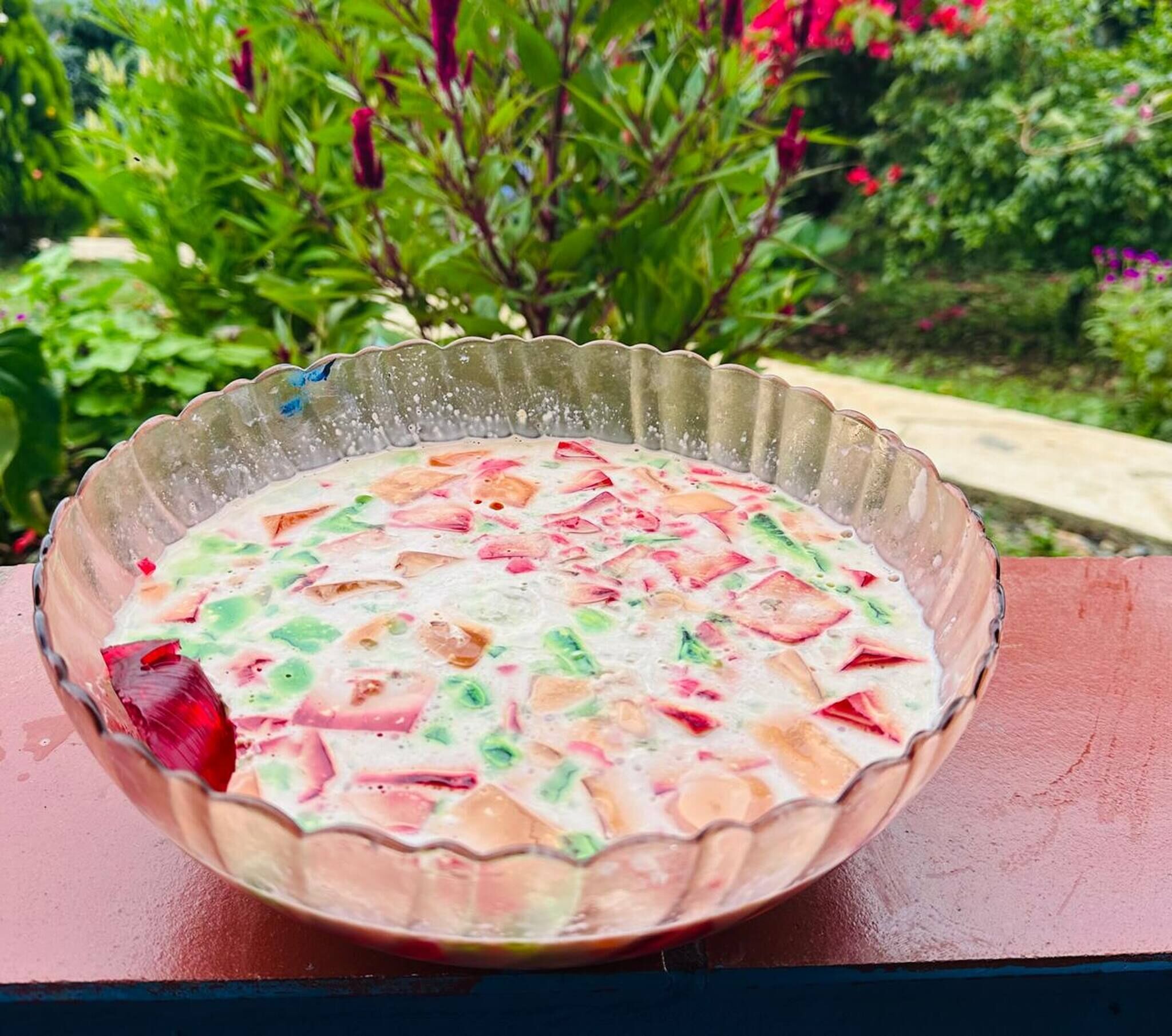 Un tazón de ensalada de frutas sobre una mesa, con vista a un jardín.