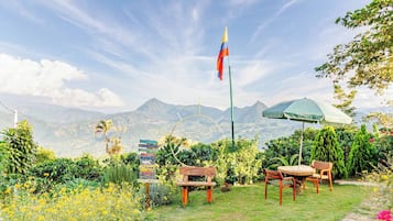 Un jardín con una bandera, un banco de madera y una mesa con sillas.