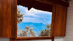 Una habitación con cama, ventana y vistas a las montañas, además de un ventilador.