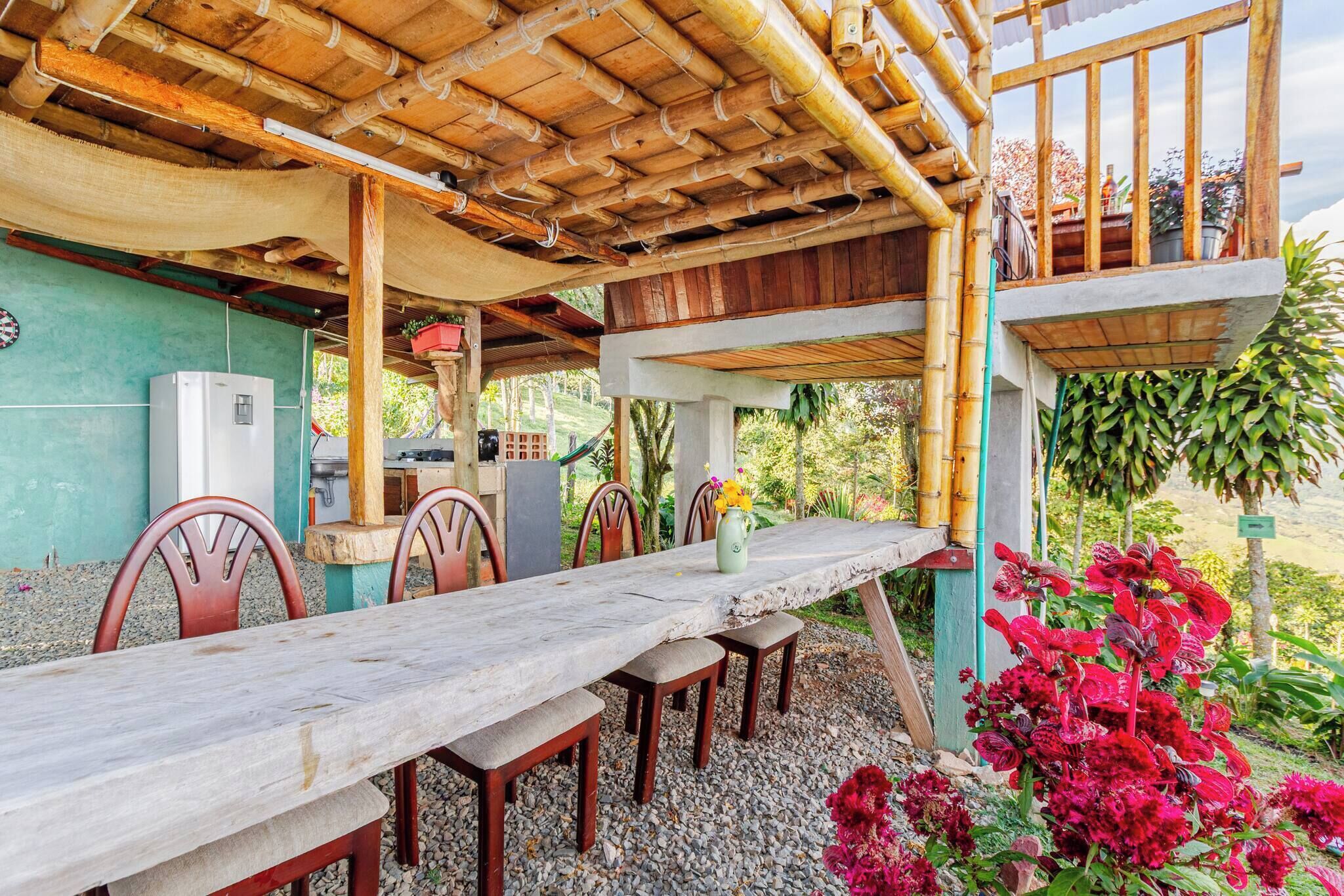 An outdoor dining area with a long table, chairs, and a covered section with a bamboo roof.