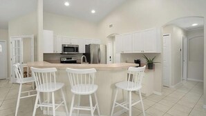 A modern kitchen with white cabinetry, a central island with bar stools, stainless steel appliances, and a potted plant. - Private Heated Pool, Sleeps 10, King Suite, Near Dining and Boating (Cape Coral)
