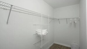 A white closet with metal shelves and a hanging rod, a white basket, and a wooden floor. - Private Heated Pool, Sleeps 10, King Suite, Near Dining and Boating (Cape Coral)