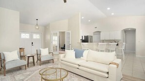 A spacious living area with a sofa, chairs, a coffee table, and a kitchen in the background. - Private Heated Pool, Sleeps 10, King Suite, Near Dining and Boating (Cape Coral)