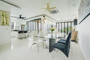 A modern kitchen with a dining area, large windows, and ceiling fans. - Panoramic Seaview Elevate Villa, Infinity Pool (Rawai)