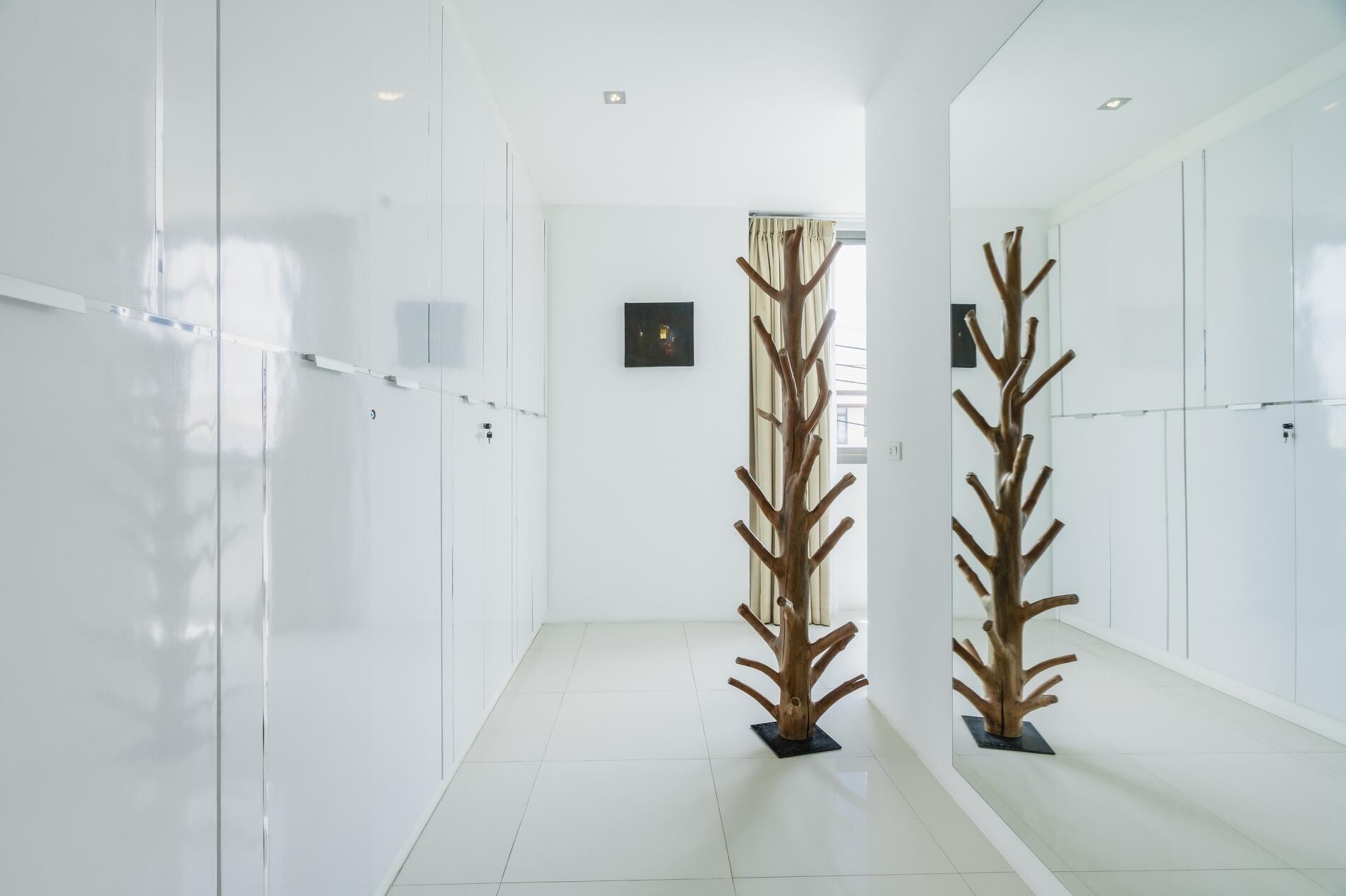 Un couloir aux murs blancs, doté d’un sol carrelé et orné de deux sculptures en bois.
