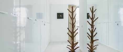 A hallway with white walls, a tiled floor, and two wooden sculptures.