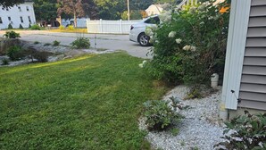 Una zona residencial con un césped cuidado, una cerca blanca y un coche estacionado.