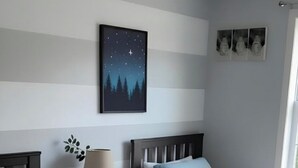 Un dormitorio con dos camas, una mesita de noche, una lámpara, un ventilador de techo, un cuadro enmarcado y una ventana.