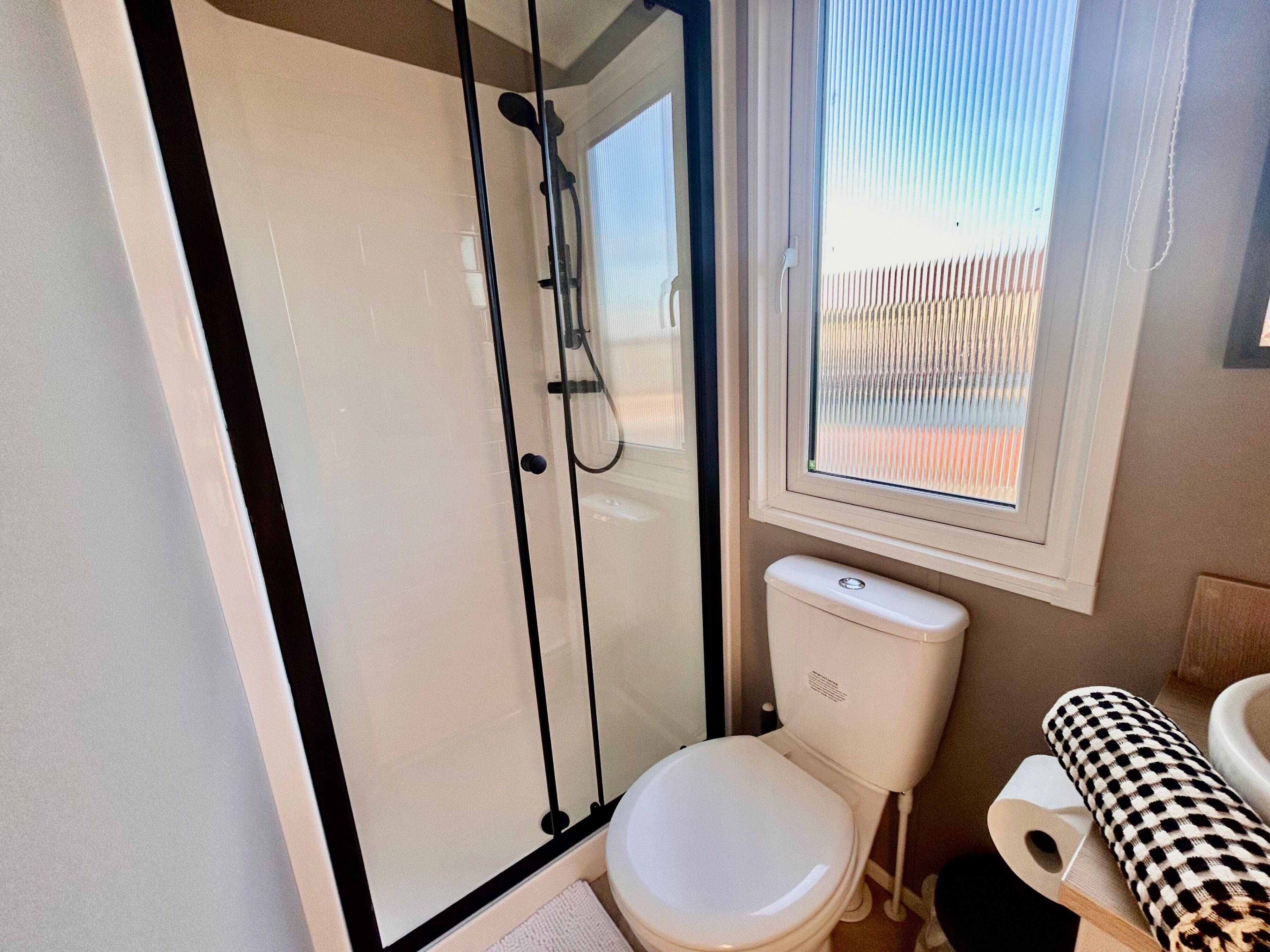 A bathroom with a glass-enclosed shower, a toilet, and a window with blinds.