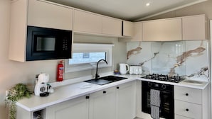 Une cuisine moderne avec des meubles blancs, un micro-ondes noir, une cuisinière à gaz et un four encastré.
