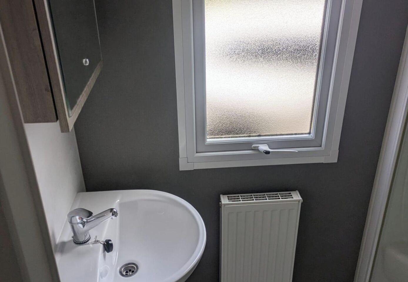 Ein Badezimmer mit einem weißen Waschbecken, einem Fenster mit Milchglas und einer weißen Heizung.