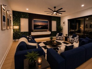 Ein modernes Wohnzimmer mit großem Fernseher, dunkelblauen Sofas, einem Couchtisch und einem Deckenventilator.