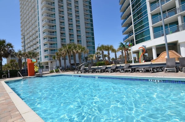 A swimming pool with lounge chairs, palm trees, and high-rise buildings in the background. - 2-bedroom condo in soothing Myrtle Beach/ Modern Decor. Stunning View-14th Flr (Myrtle Beach)