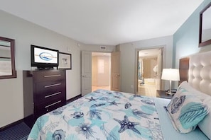 A hotel room with a bed, a television, a dresser, and a bathroom visible through an open door. - 2-bedroom condo in soothing Myrtle Beach/ Modern Decor. Stunning View-14th Flr (Myrtle Beach)