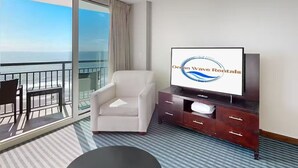 Ein Hotelzimmer mit Balkon, einem Fernseher, einem weißen Sessel und einer dunklen Holzkommode.
