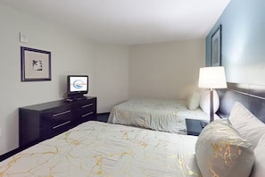 Ein Hotelzimmer mit zwei Betten, einem Fernseher, einem Schreibtisch und einer Lampe.