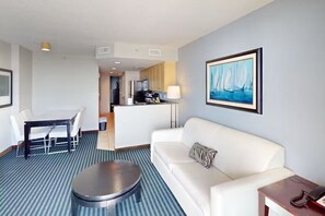 A hotel room with a white sofa, a round coffee table, a dining table with chairs, a kitchen area, and a painting of sailboats on the wall. - 2-bedroom condo in soothing Myrtle Beach/ Modern Decor. Stunning View-14th Flr (Myrtle Beach)
