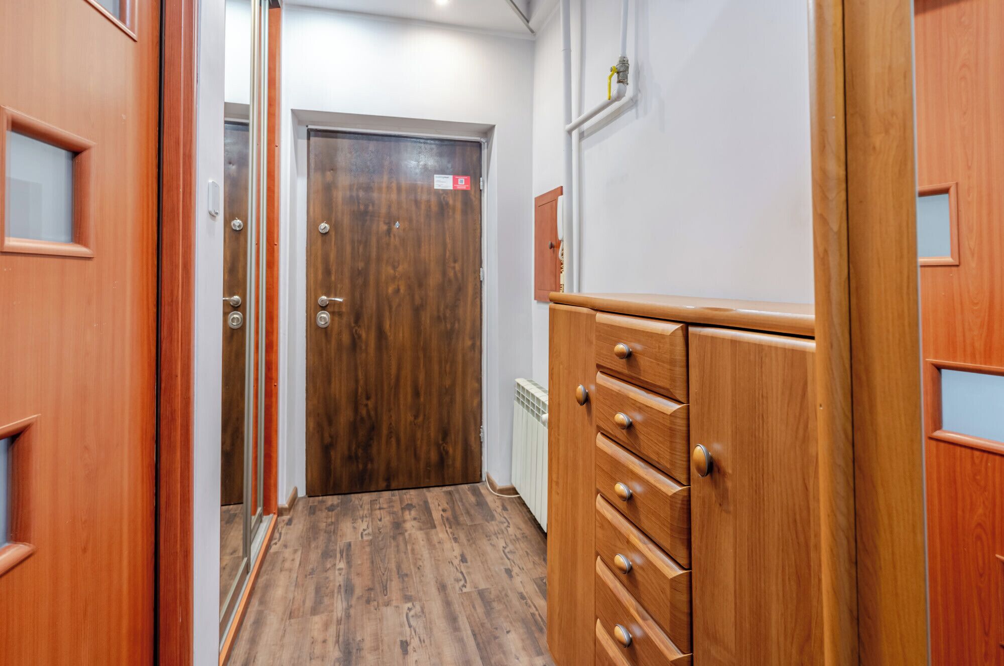 A hallway with wooden doors, a radiator, and a wooden cabinet with drawers.