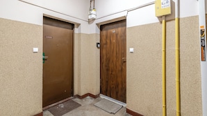 Un couloir étroit avec deux portes en bois, un tuyau jaune et une petite marche menant à une porte.