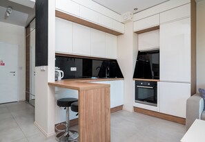 A modern kitchen with white cabinets, a wooden countertop, a black stove, and a black chair. - Pieskowa Skała 15 Prestige Apartment (Warszawa)
