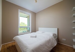 Ein Schlafzimmer mit einem Bett, einem Fenster und Blick auf Grünfläche.