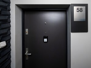 Eine schwarze Tür mit Schlüsselloch, Klingel und Kartenlesegerät. Eine Nummernschild mit der Aufschrift '58' ist an der Wand befestigt.