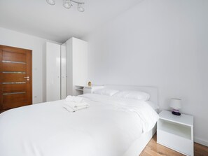 Ein modernes Schlafzimmer mit einem großen Bett, einer Holztür, einem weißen Kleiderschrank und einem Nachttisch mit Lampe.