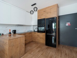 Eine moderne Küche mit Holzschränken, einem schwarzen Kühlschrank und einem eingebauten Backofen.