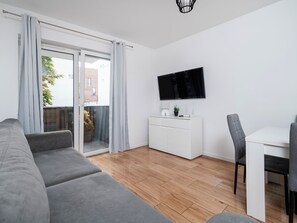 Ein modernes Wohnzimmer mit einem grauen Sofa, einer weißen Kommode, einem Flachbildfernseher und einem Essbereich mit Tisch und Stühlen.