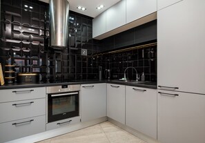 Une cuisine moderne avec des meubles gris, une hotte en acier inoxydable et un four encastré.