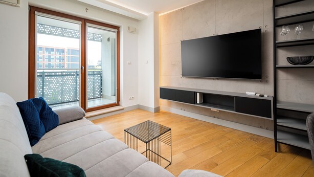 Un saló modern amb una televisió plana gran, un sofà i un balcó amb vista a edificis.