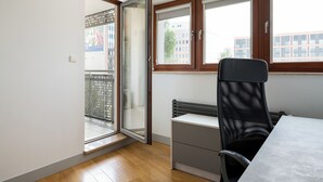 Habitació amb porta de vidre corredissa, radiador, escriptori amb cadira i finestra amb persianes.